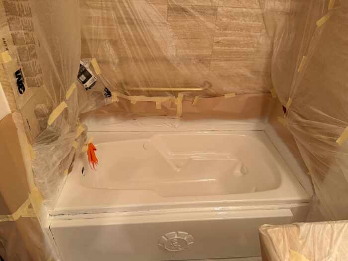 Bathtub refinishing in progress with surrounding plastic masking