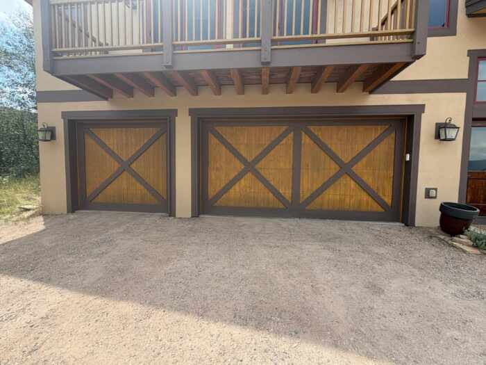Finished carriage-style garage doors with wood panels and dark trim